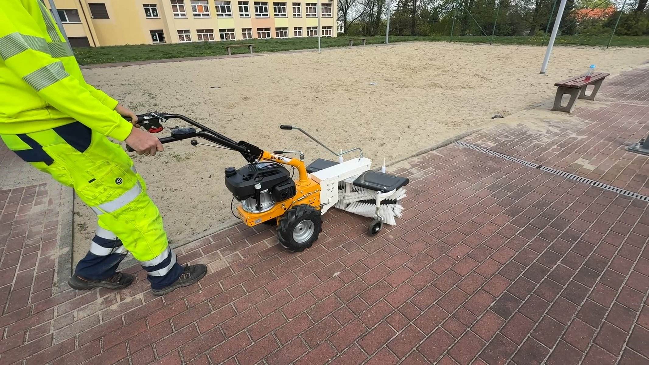 Zamiatarka spalinowa czyszcząca kostkę brukową przy piaskownicy — sprzątanie otoczenia placu zabaw