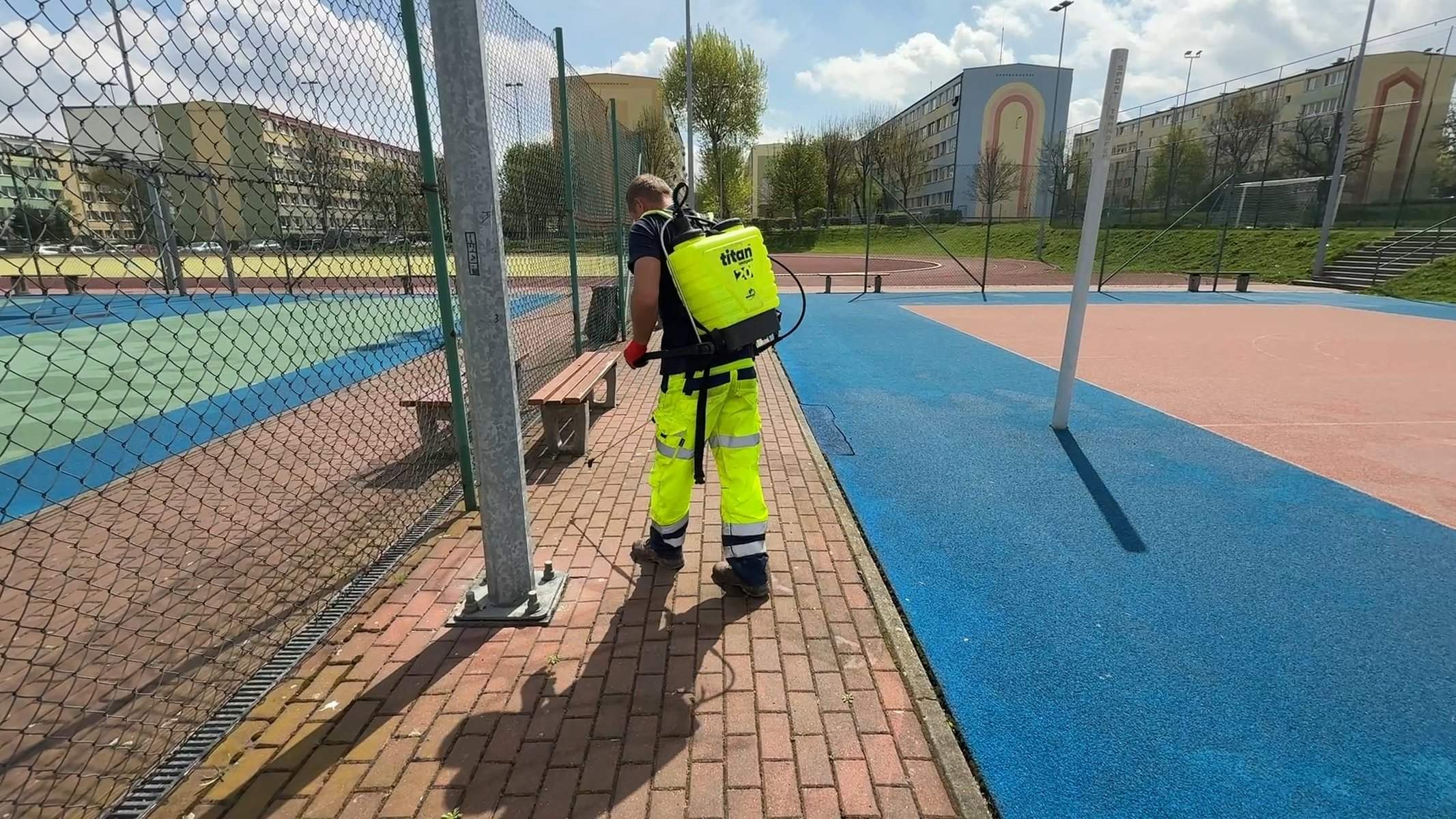 Odchwaszczanie nawierzchni opryskiwaczem plecakowym między boiskami — utrzymanie kompleksów sportowych