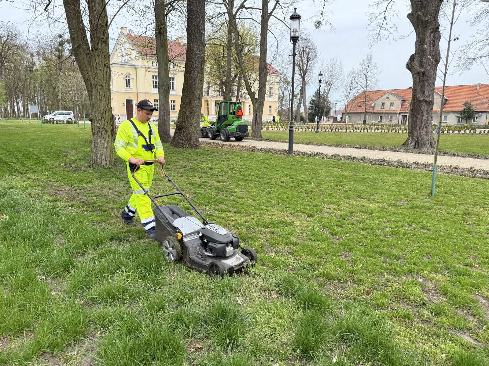 Pracownik kosi trawę kosiarką pchaną w zabytkowym parku pałacowym — utrzymanie zieleni parkowej