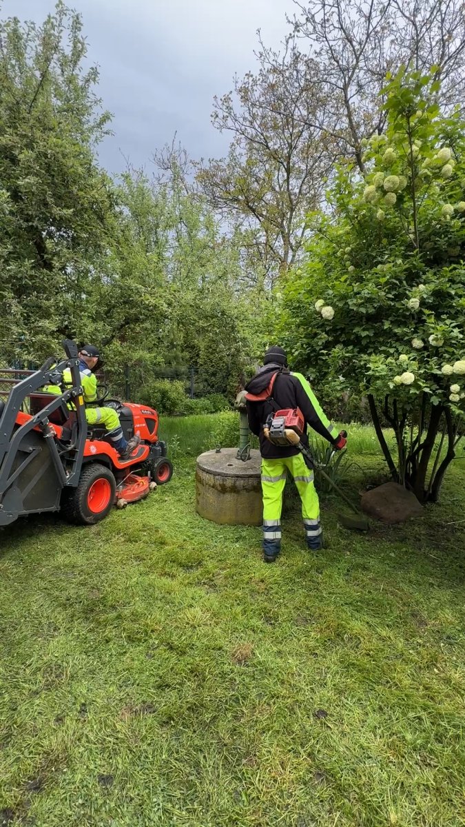 Koszenie trawy w sadzie — traktor ogrodowy i wykaszarka żyłkowa przy studni
