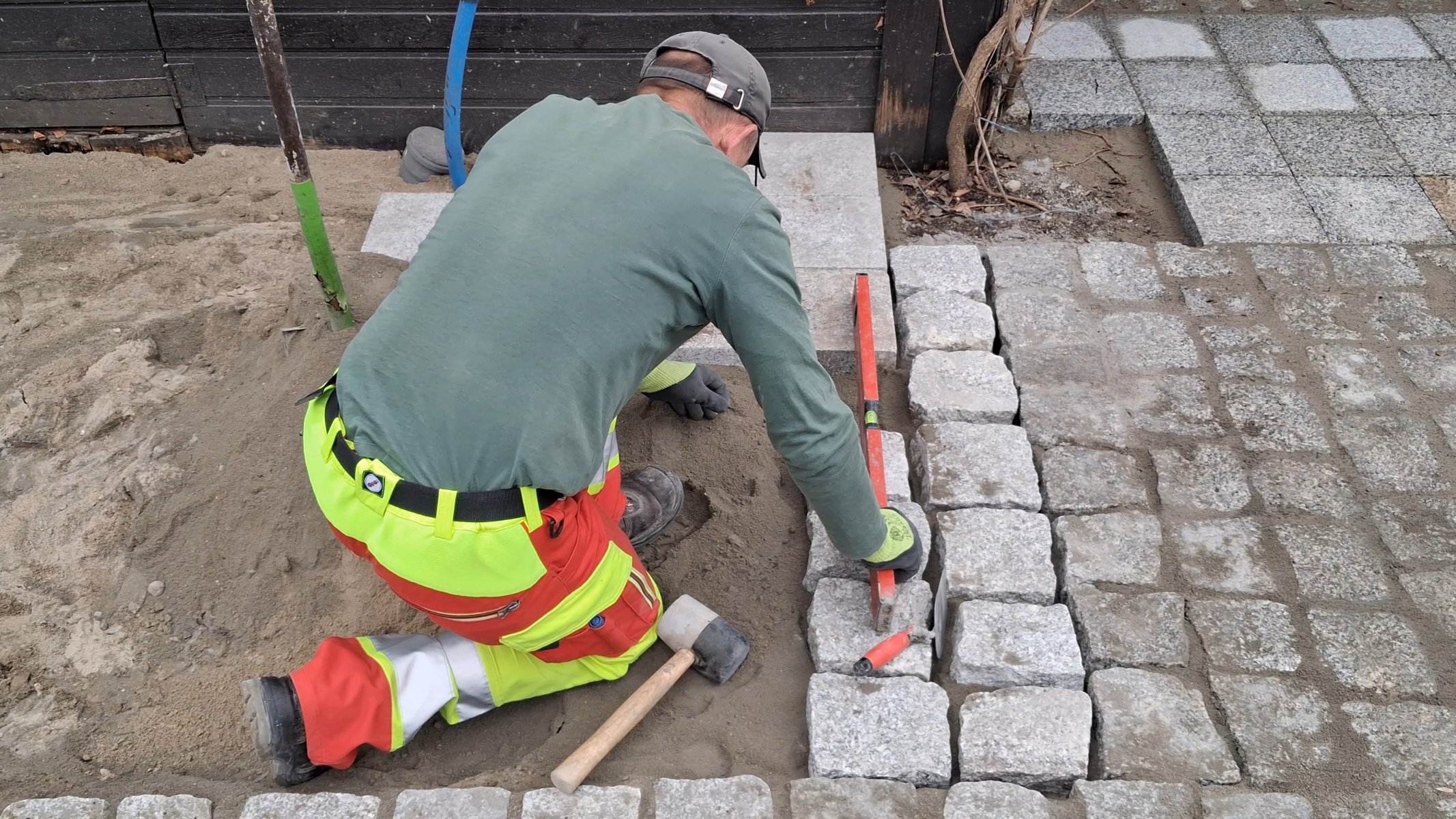 Brukarz wyrównuje poziomicą kostkę granitową przy płytach — układanie kostki granitowej Kalisz