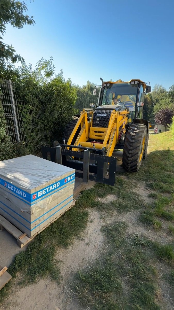 Koparko-ładowarka transportuje paletę kostki brukowej na budowę