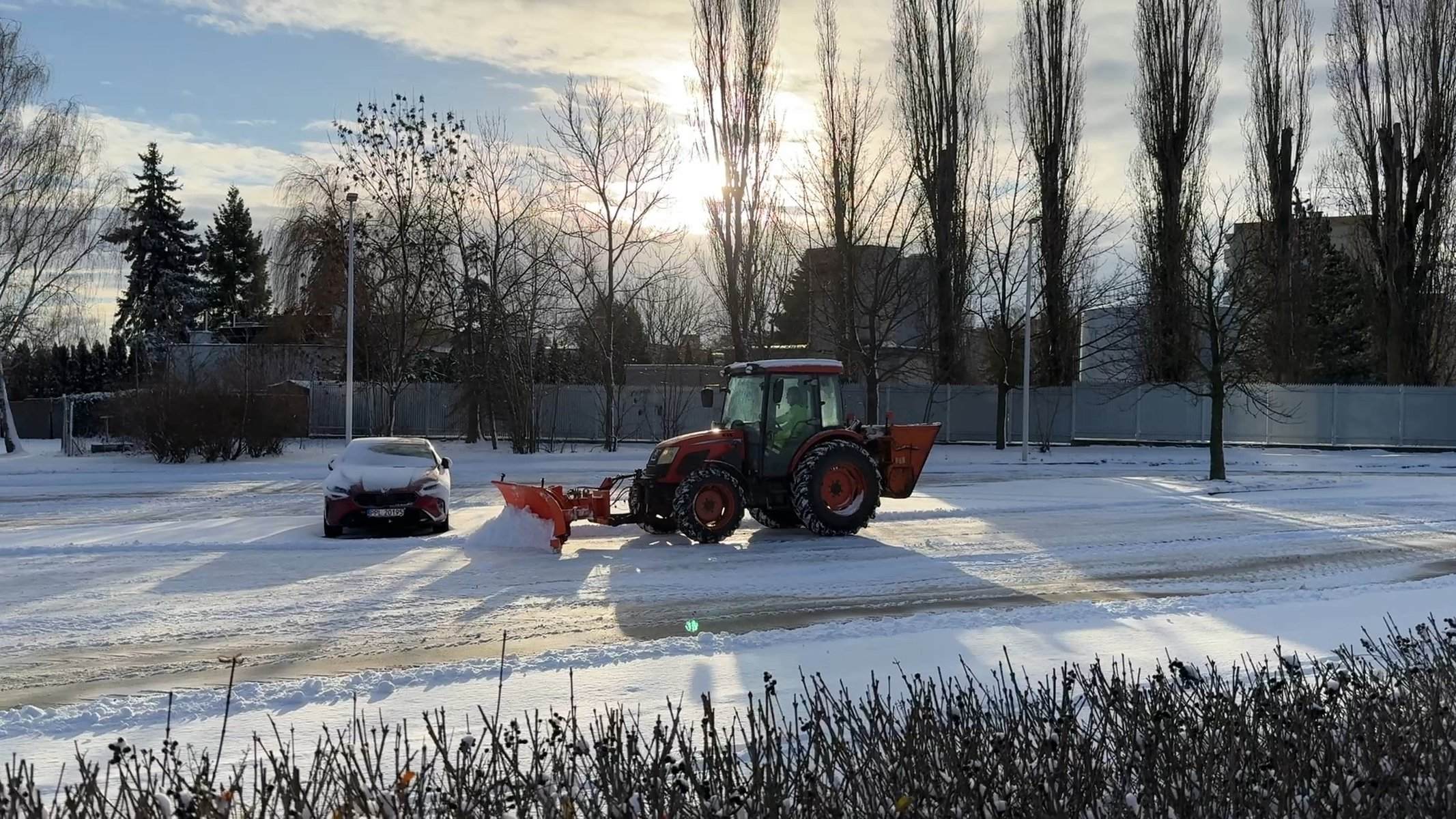 Ciągnik z pługiem odśnieża parking o świcie — odśnieżanie parkingów firmowych